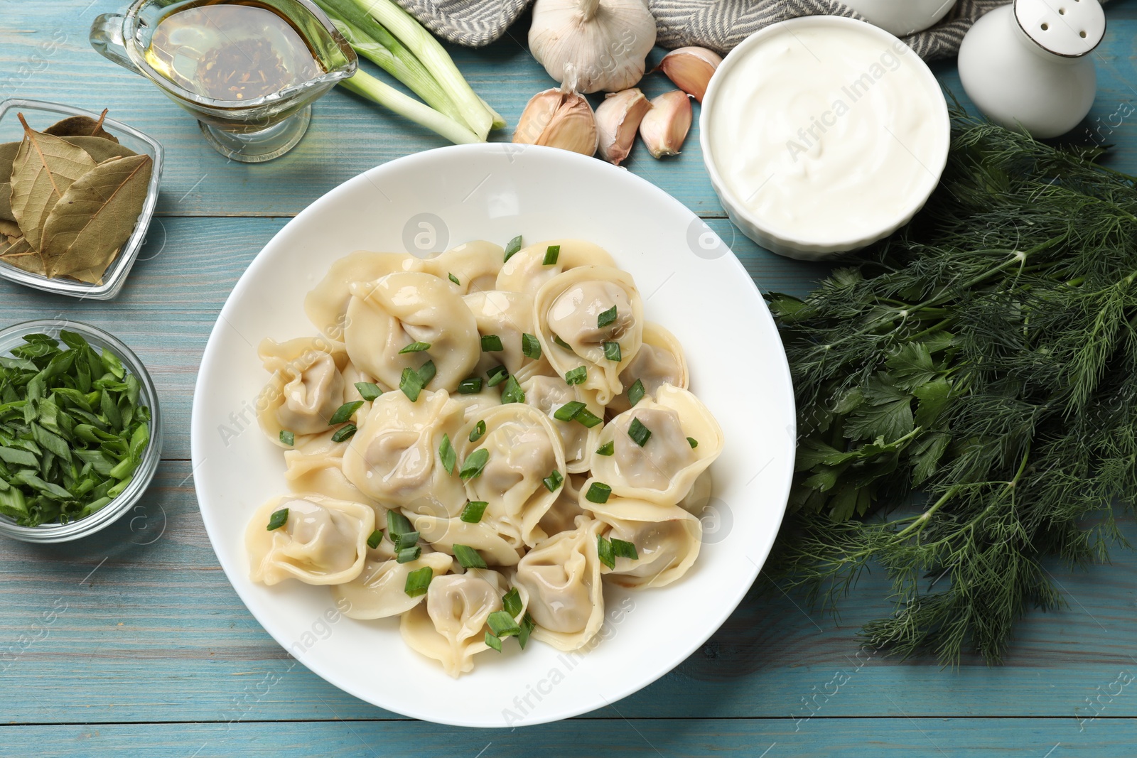 Photo of Delicious pelmeni with green onion served on blue wooden table, flat lay