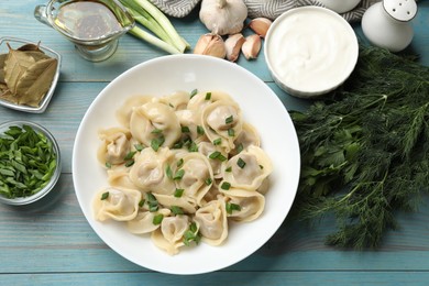 Photo of Delicious pelmeni with green onion served on blue wooden table, flat lay