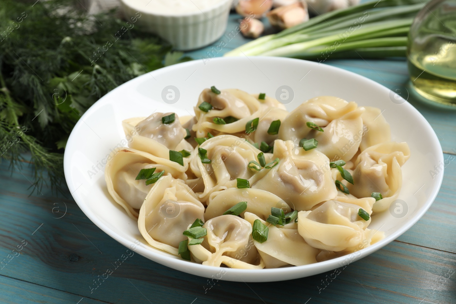 Photo of Delicious pelmeni with green onion served on blue wooden table, closeup