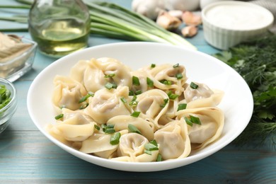 Photo of Delicious pelmeni with green onion served on blue wooden table, closeup