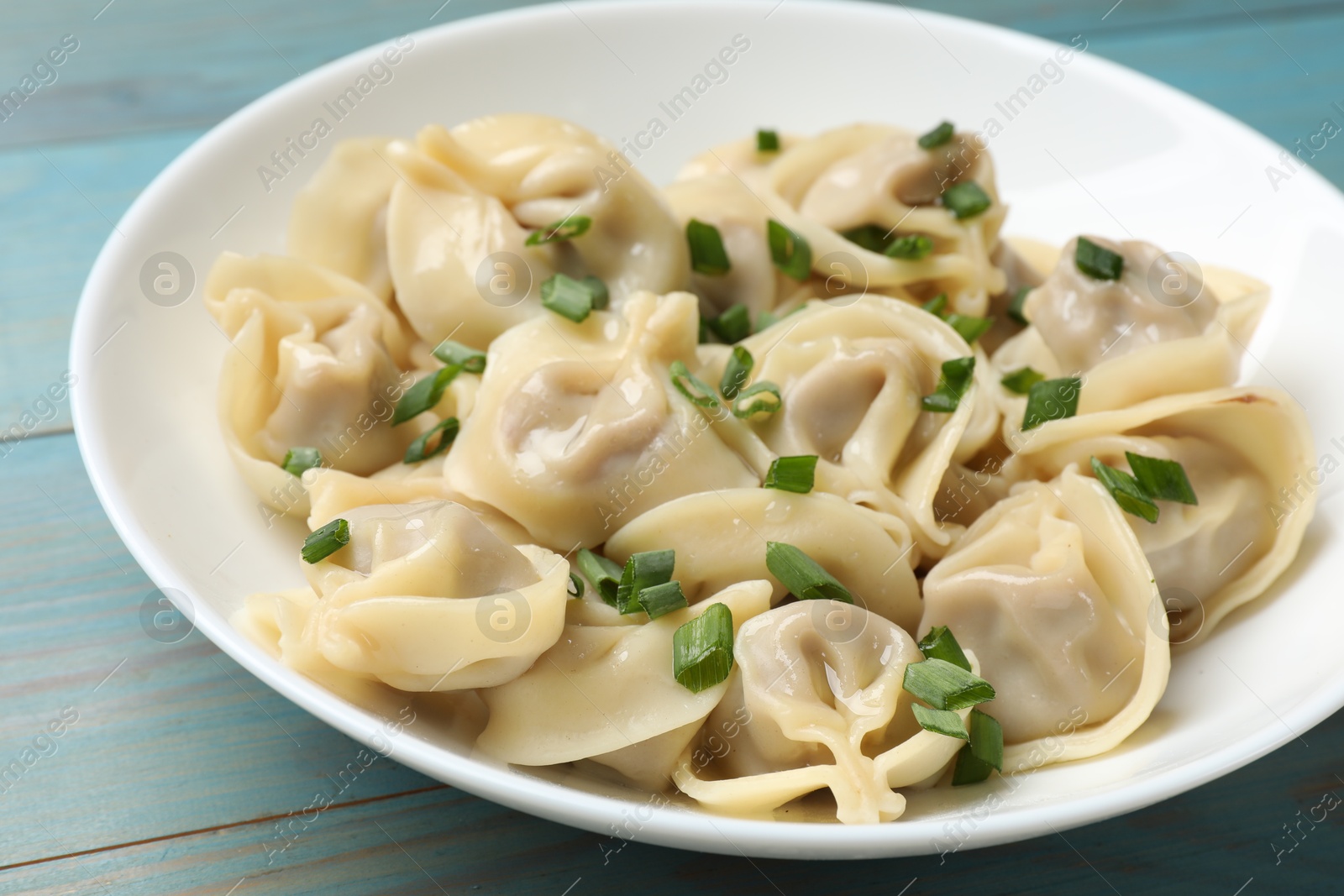 Photo of Delicious pelmeni with green onion on blue wooden table, closeup