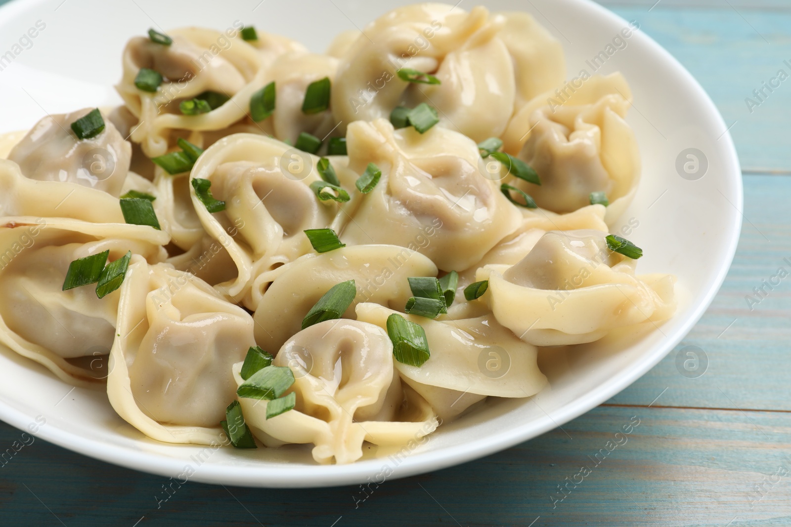 Photo of Delicious pelmeni with green onion on blue wooden table, closeup