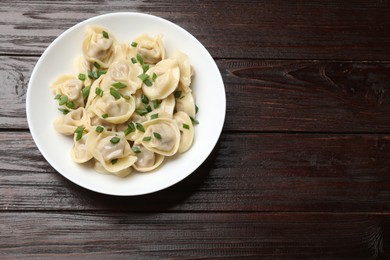 Photo of Delicious pelmeni with green onion on wooden table, top view. Space for text