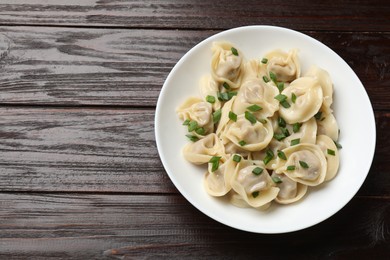 Photo of Delicious pelmeni with green onion on wooden table, top view. Space for text