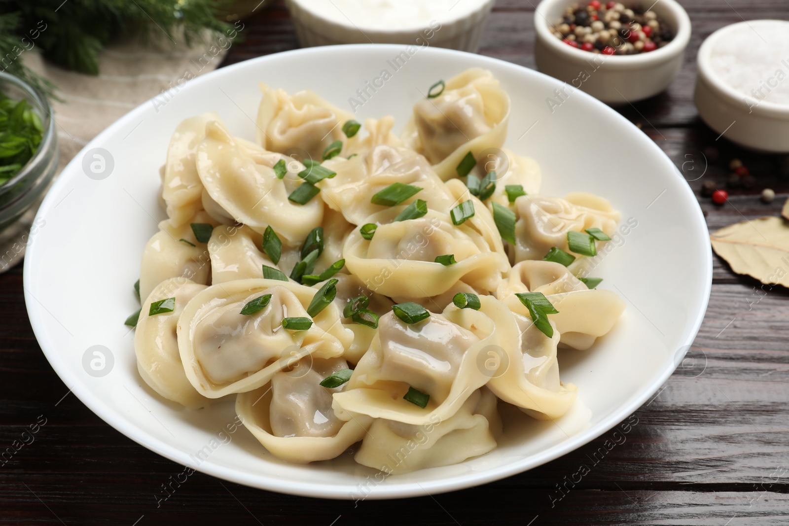 Photo of Delicious pelmeni with green onion served on wooden table, closeup