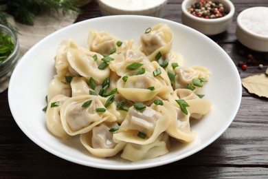 Photo of Delicious pelmeni with green onion served on wooden table, closeup