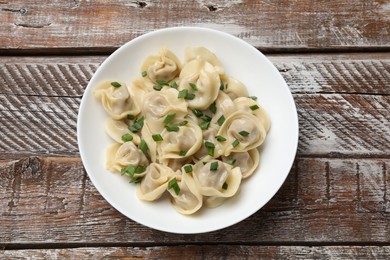 Photo of Delicious pelmeni with green onion on wooden table, top view