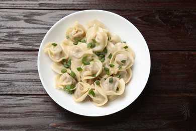 Photo of Delicious pelmeni with green onion on wooden table, top view