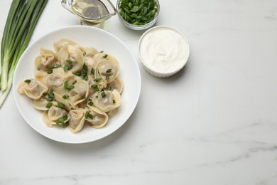 Photo of Delicious pelmeni with green onion served on white marble table, flat lay