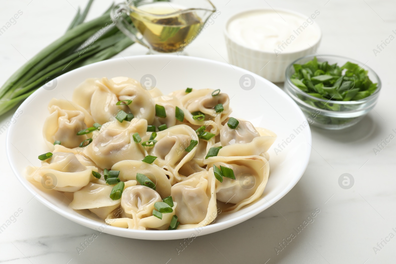 Photo of Delicious pelmeni with green onion served on white table, closeup