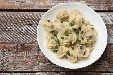 Photo of Delicious pelmeni with green onion on wooden table, top view. Space for text