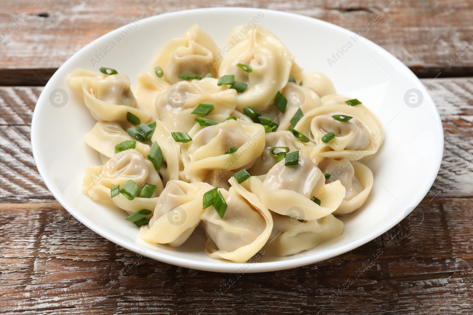 Photo of Delicious pelmeni with green onion on wooden table, closeup