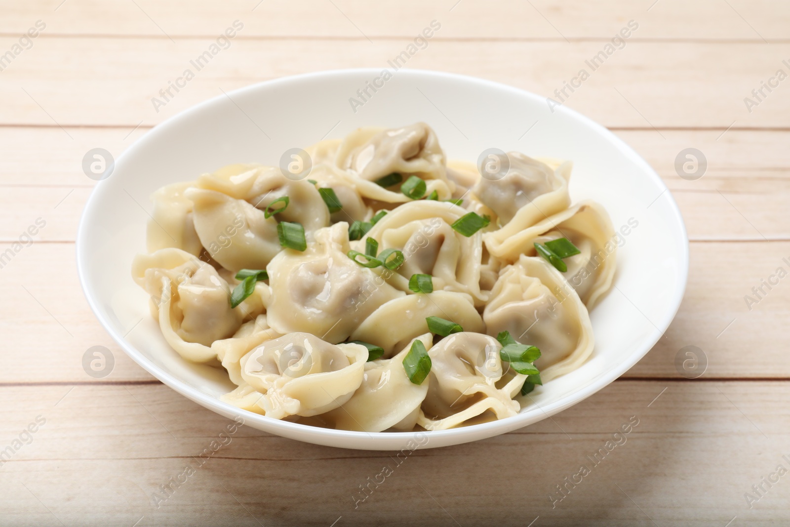 Photo of Delicious pelmeni with green onion on white wooden table