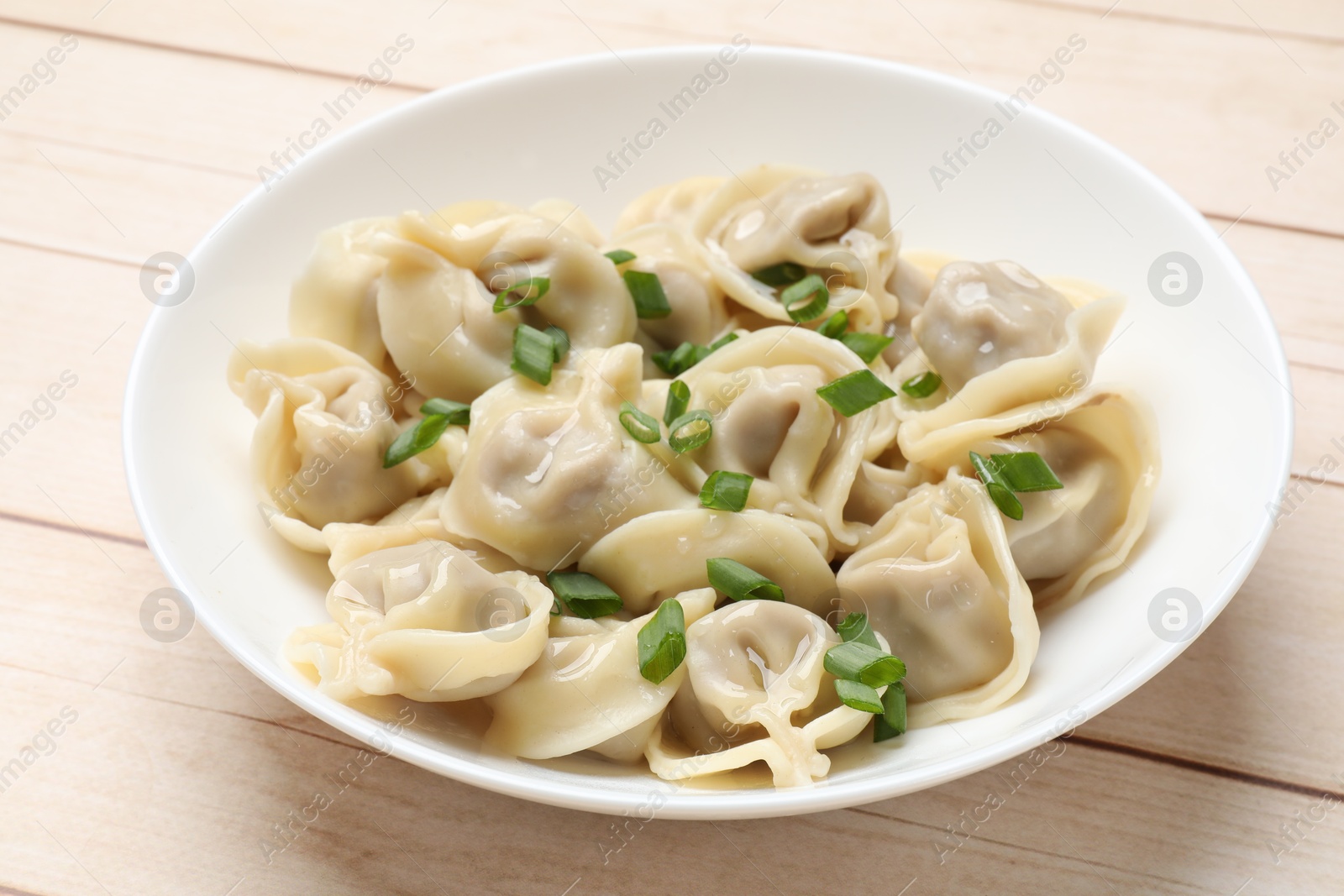 Photo of Delicious pelmeni with green onion on white wooden table, closeup