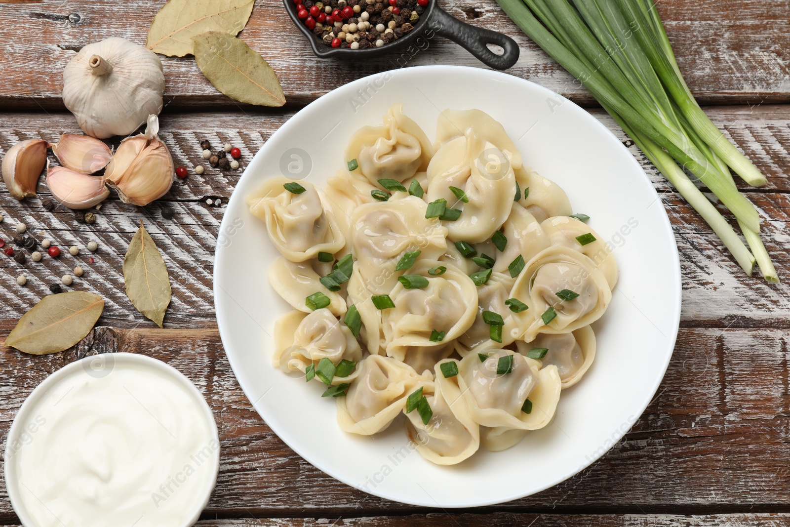 Photo of Delicious pelmeni with green onion served on wooden table, flat lay