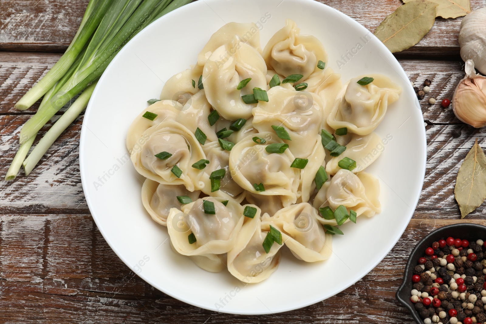 Photo of Delicious pelmeni with green onion served on wooden table, flat lay