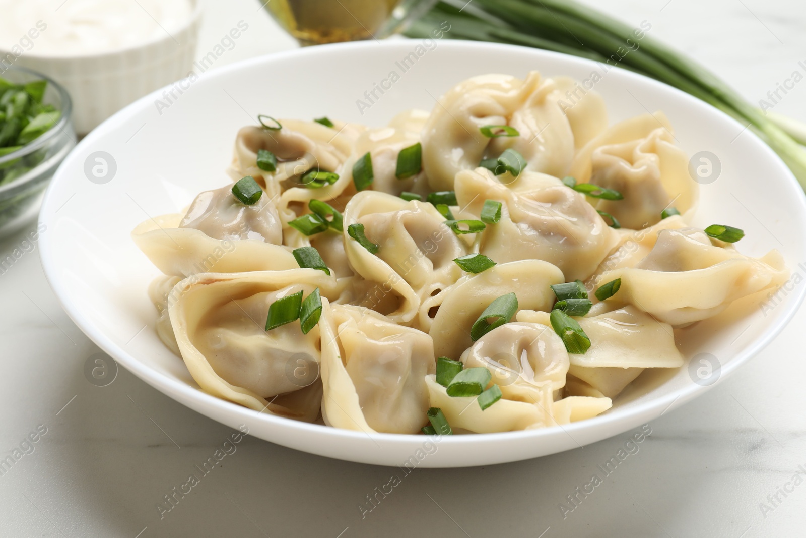 Photo of Delicious pelmeni with green onion on white table, closeup