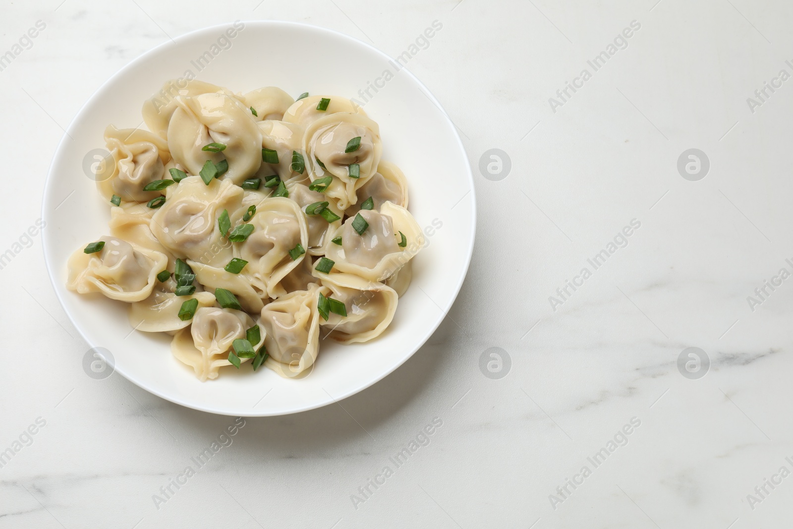 Photo of Delicious pelmeni with green onion on white marble table, top view. Space for text