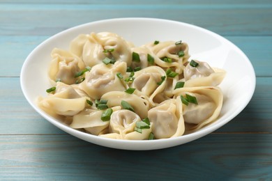 Photo of Delicious pelmeni with green onion on blue wooden table, closeup