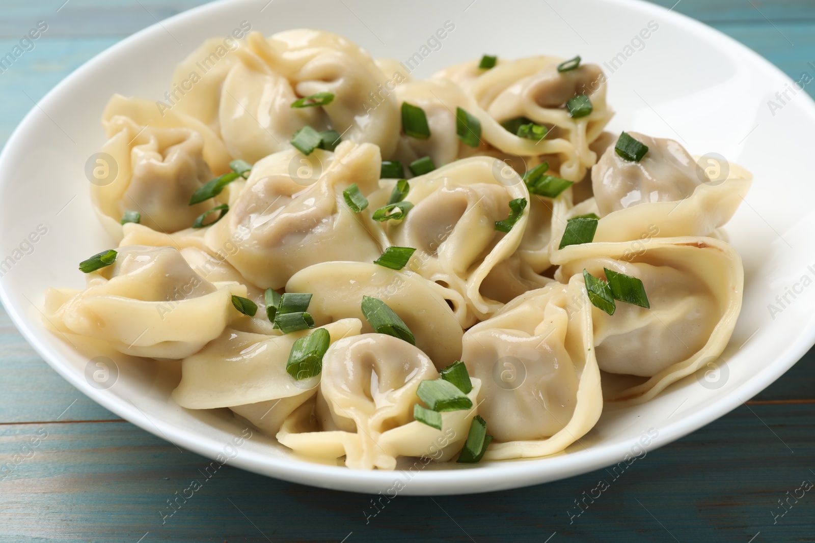 Photo of Delicious pelmeni with green onion on blue wooden table, closeup