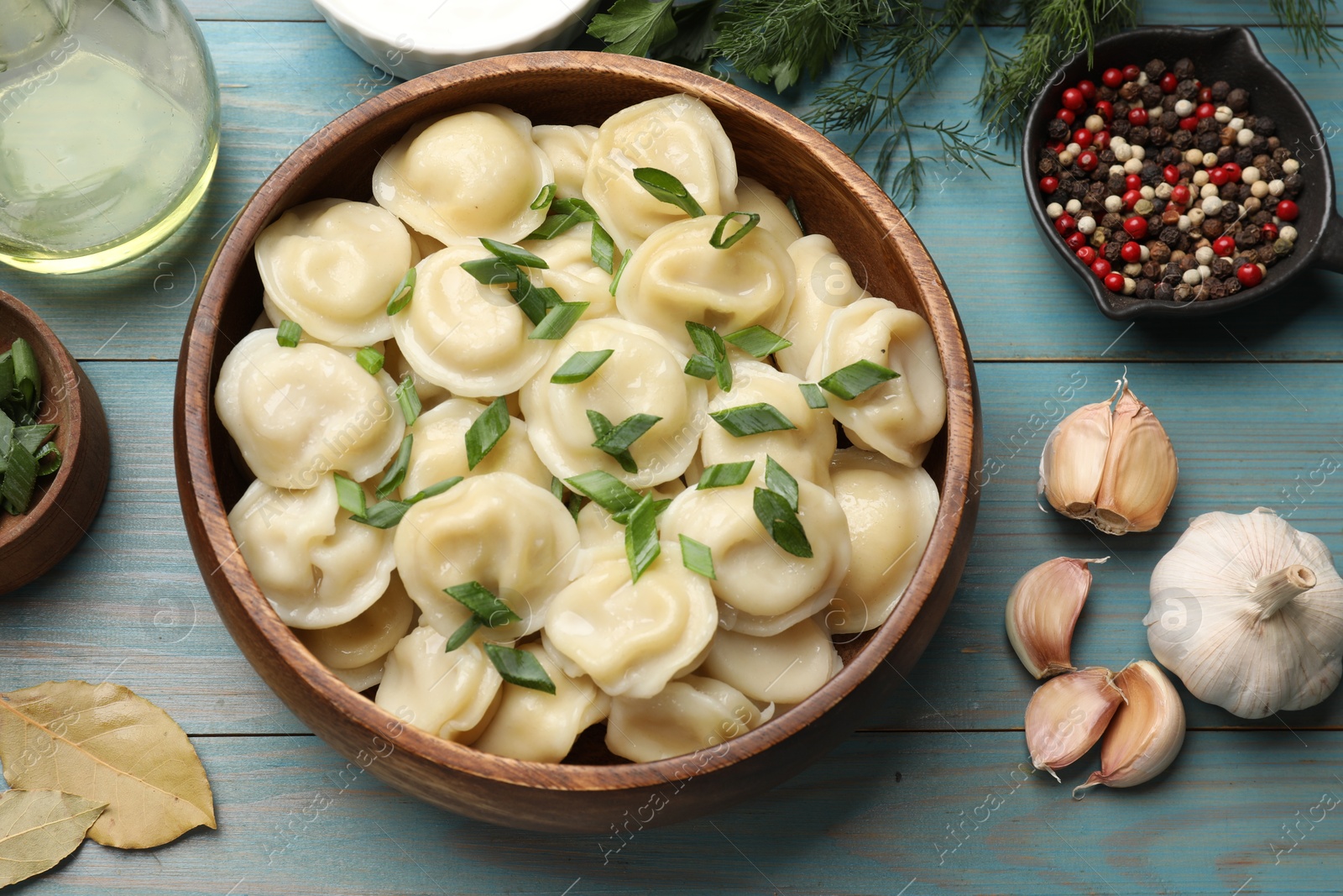 Photo of Delicious pelmeni with green onion served on light blue wooden table, flat lay