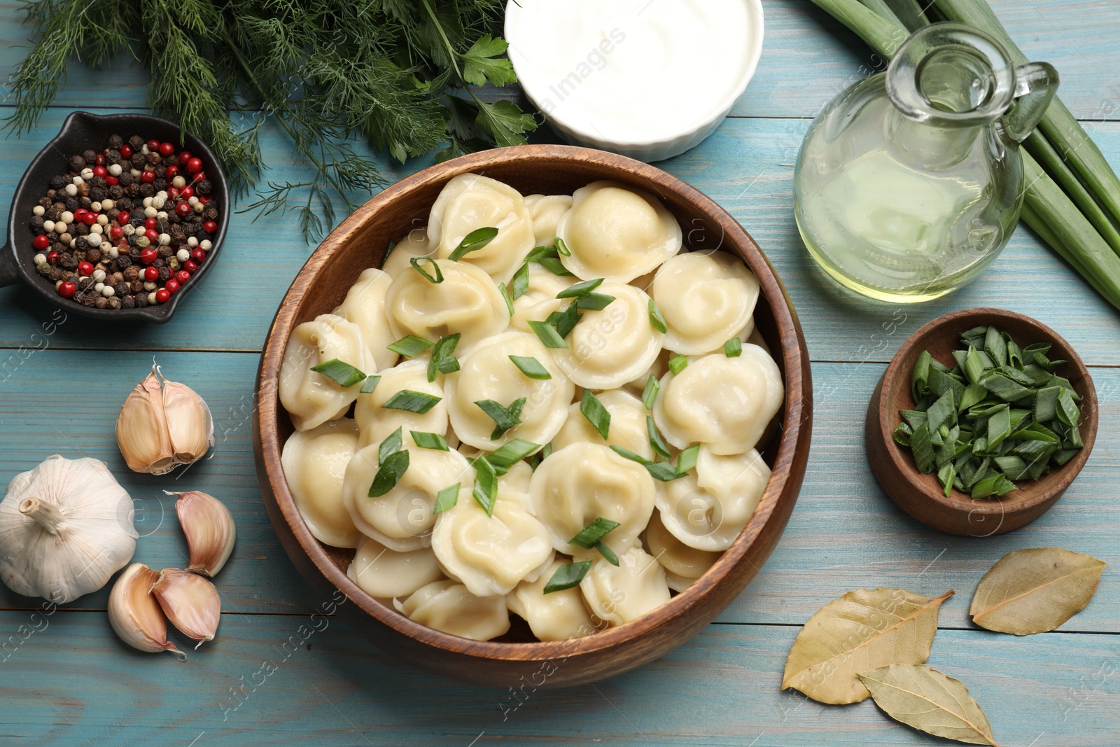 Photo of Delicious pelmeni with green onion served on light blue wooden table, flat lay