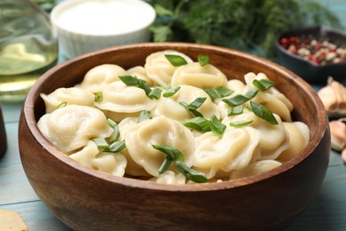 Delicious pelmeni with green onion in bowl on light blue wooden table, closeup