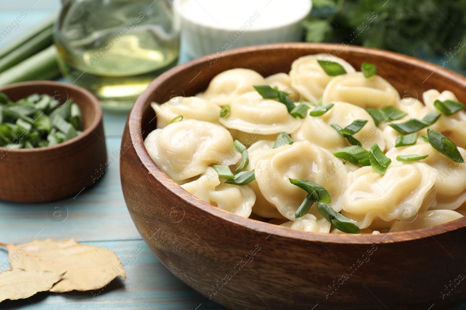 Photo of Delicious pelmeni with green onion in bowl on light blue wooden table, closeup