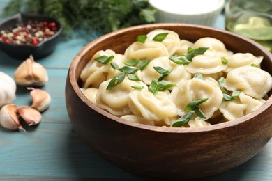 Photo of Delicious pelmeni with green onion in bowl on light blue wooden table, closeup