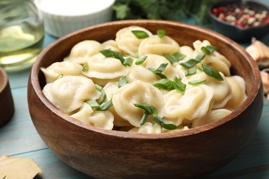 Delicious pelmeni with green onion in bowl on light blue wooden table, closeup