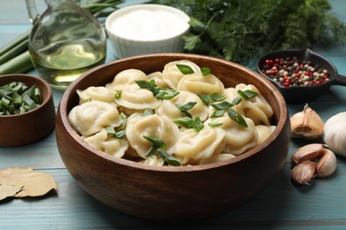 Delicious pelmeni with green onion in bowl on light blue wooden table, closeup