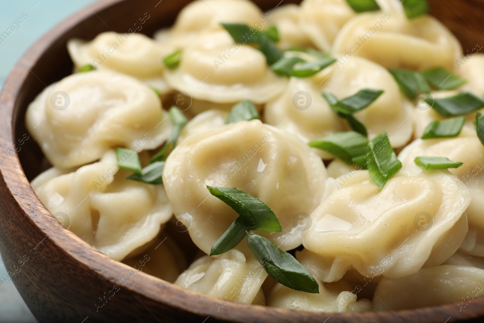 Photo of Delicious pelmeni with green onion in bowl, closeup