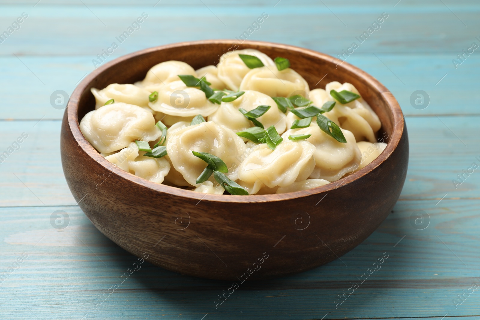 Photo of Delicious pelmeni with green onion in bowl on light blue wooden table