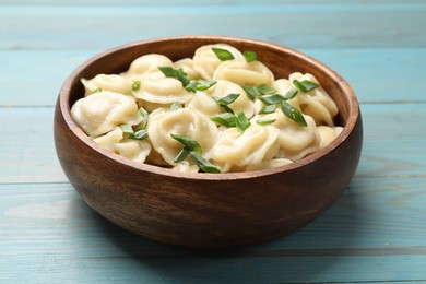 Photo of Delicious pelmeni with green onion in bowl on light blue wooden table