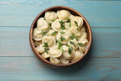 Photo of Delicious pelmeni with green onion in bowl on light blue wooden table, top view