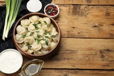 Delicious pelmeni with green onion served on wooden table, flat lay. Space for text