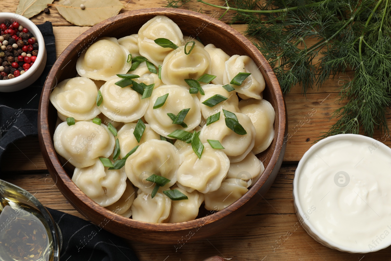 Photo of Delicious pelmeni with green onion served on wooden table, flat lay