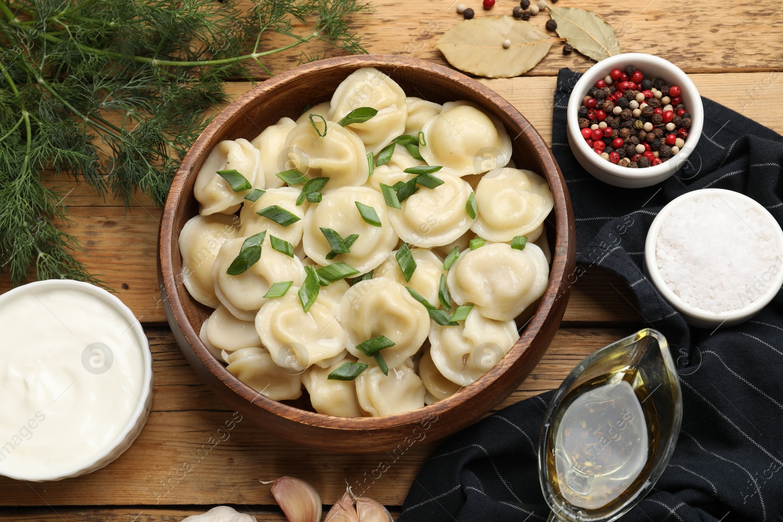 Photo of Delicious pelmeni with green onion served on wooden table, flat lay