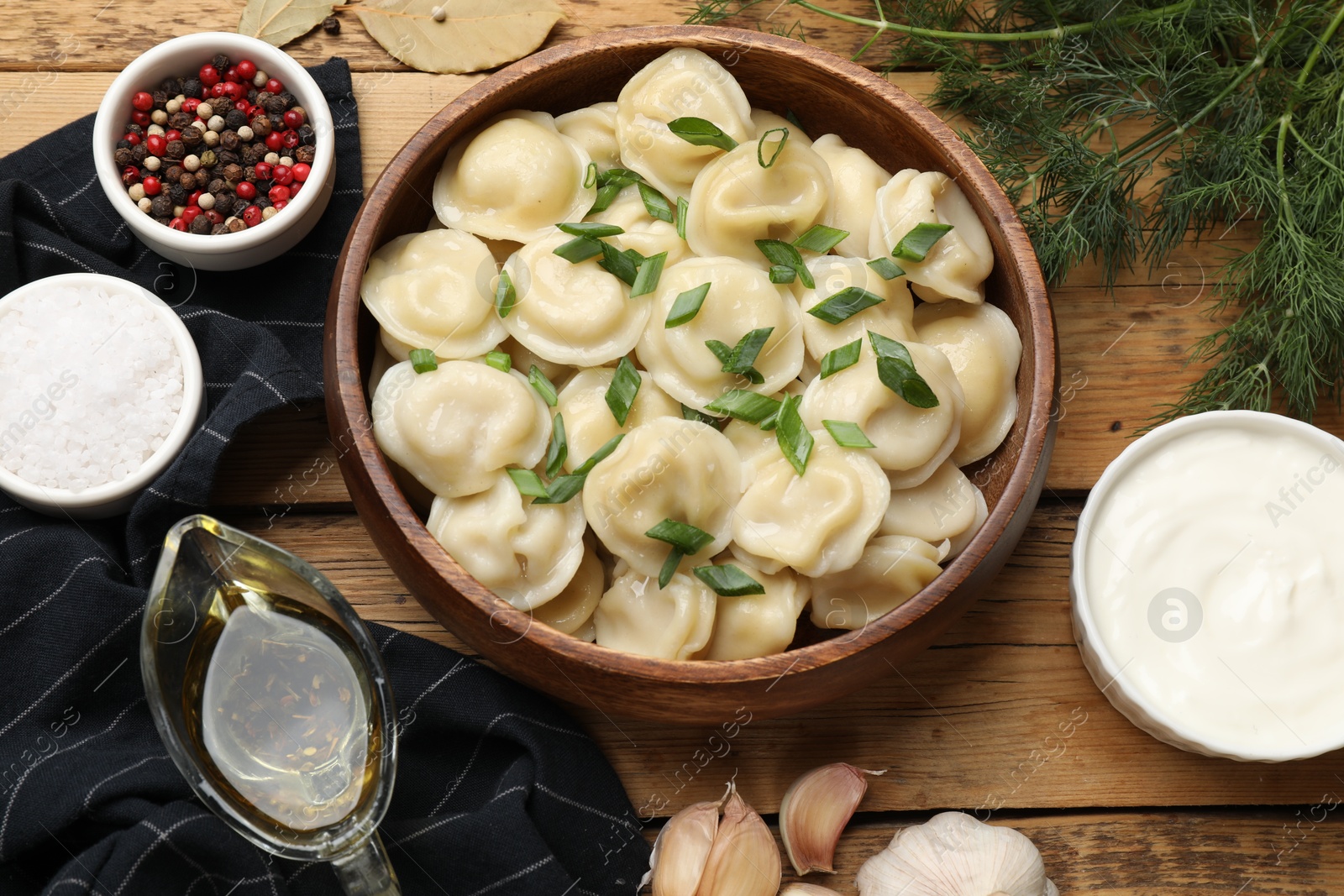 Photo of Delicious pelmeni with green onion served on wooden table, flat lay