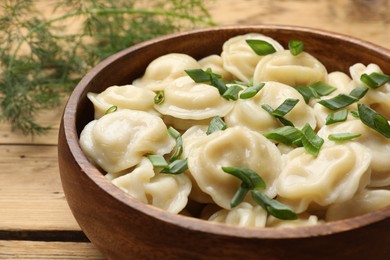 Photo of Delicious pelmeni with green onion in bowl on wooden table, closeup