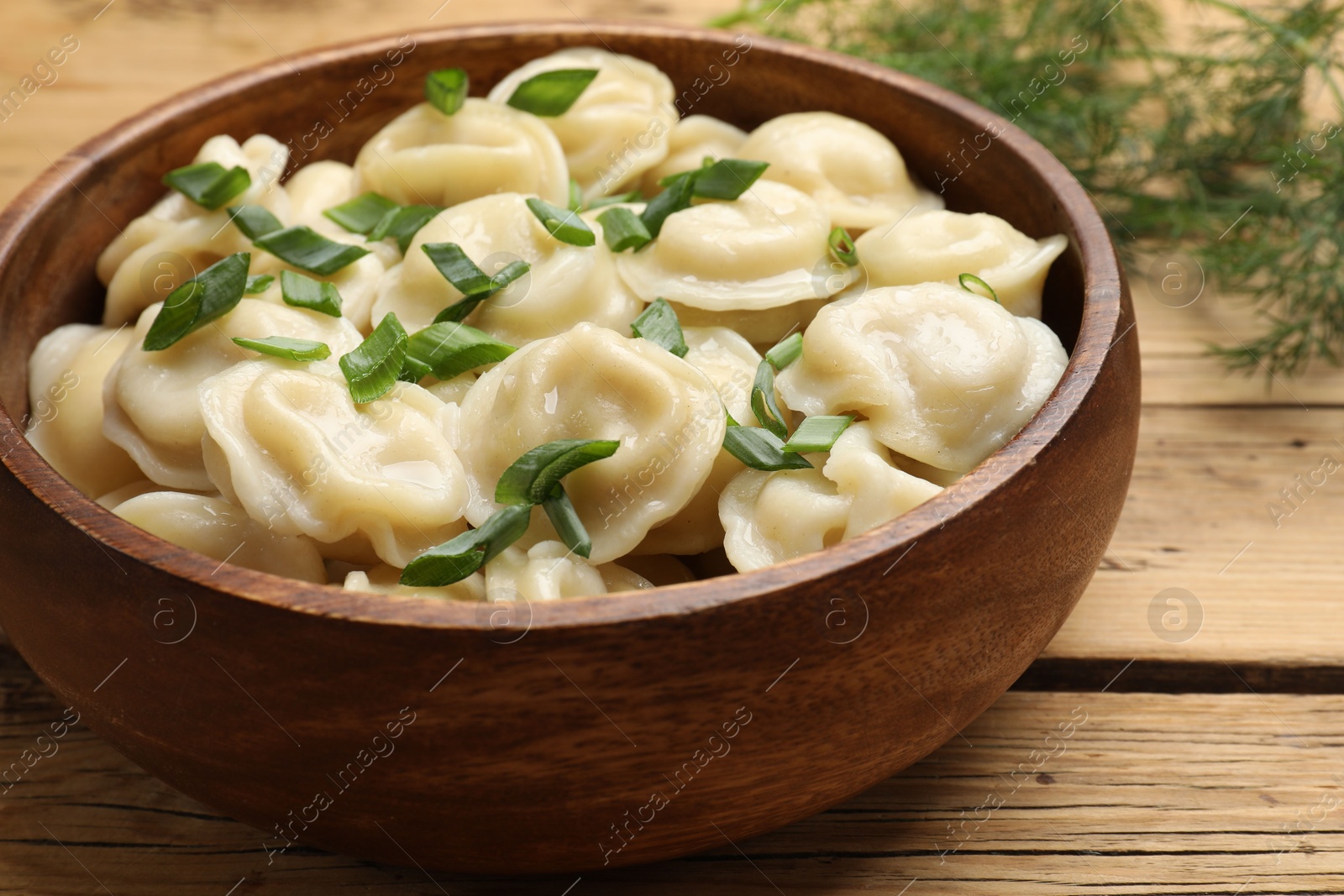 Photo of Delicious pelmeni with green onion in bowl on wooden table, closeup