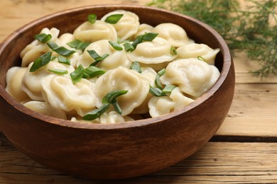 Photo of Delicious pelmeni with green onion in bowl on wooden table, closeup