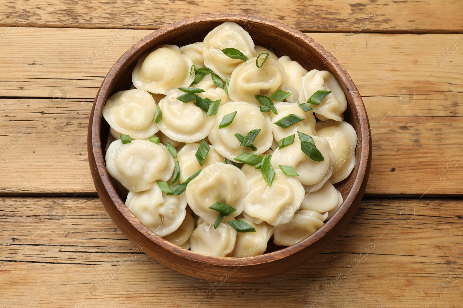 Photo of Delicious pelmeni with green onion in bowl on wooden table, top view