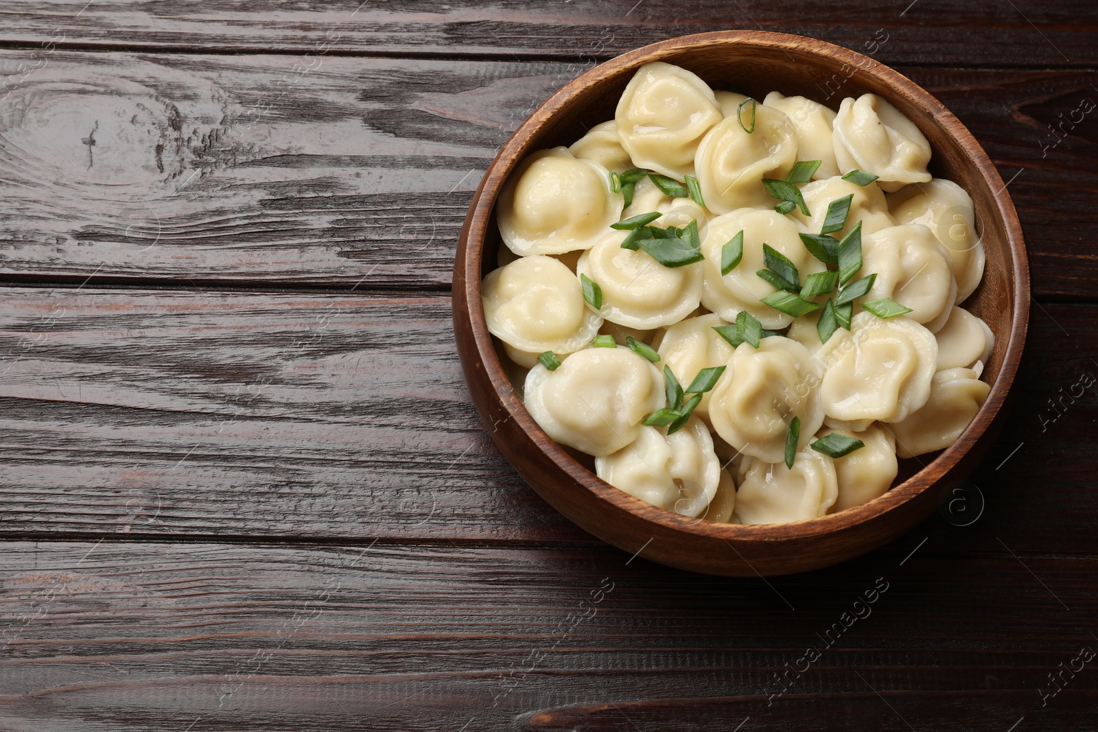 Photo of Delicious pelmeni with green onion in bowl on wooden table, top view. Space for text