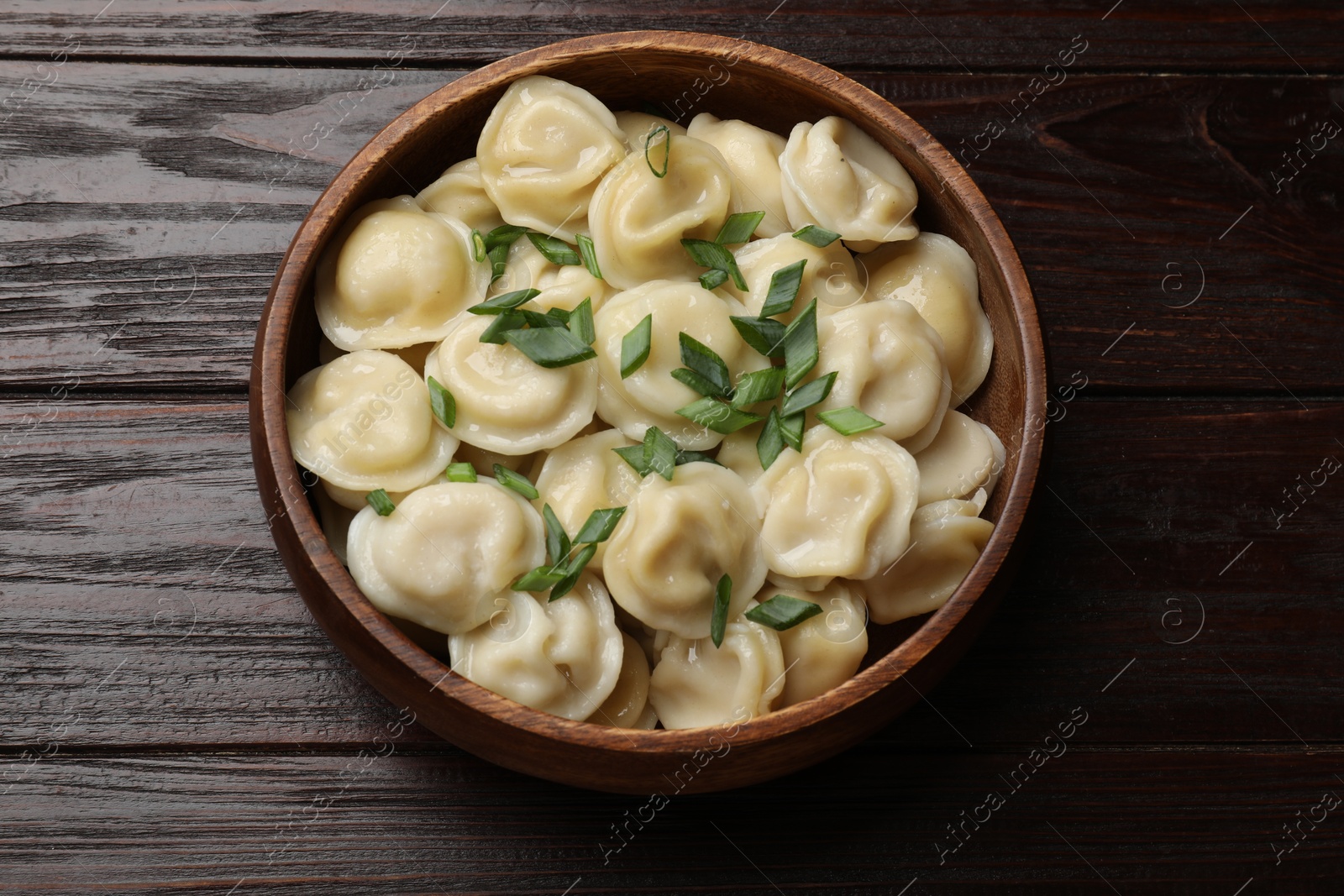 Photo of Delicious pelmeni with green onion in bowl on wooden table, top view