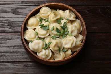 Photo of Delicious pelmeni with green onion in bowl on wooden table, top view