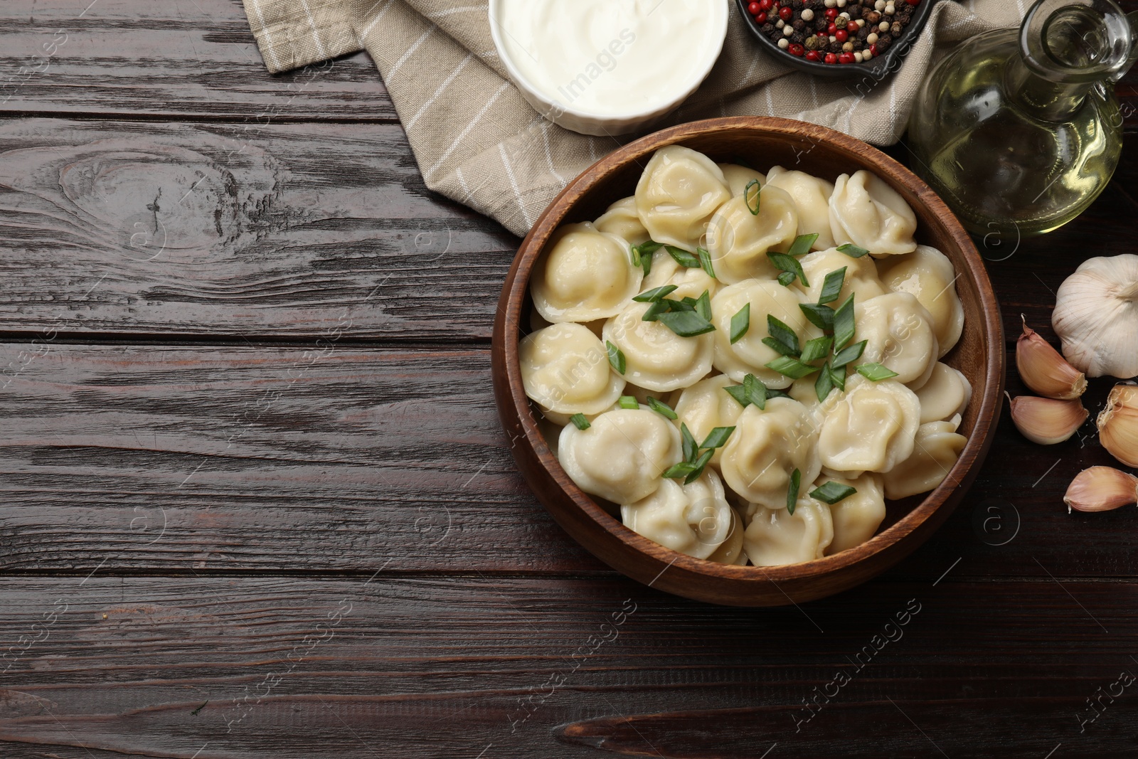 Photo of Delicious pelmeni with green onion served on wooden table, flat lay. Space for text