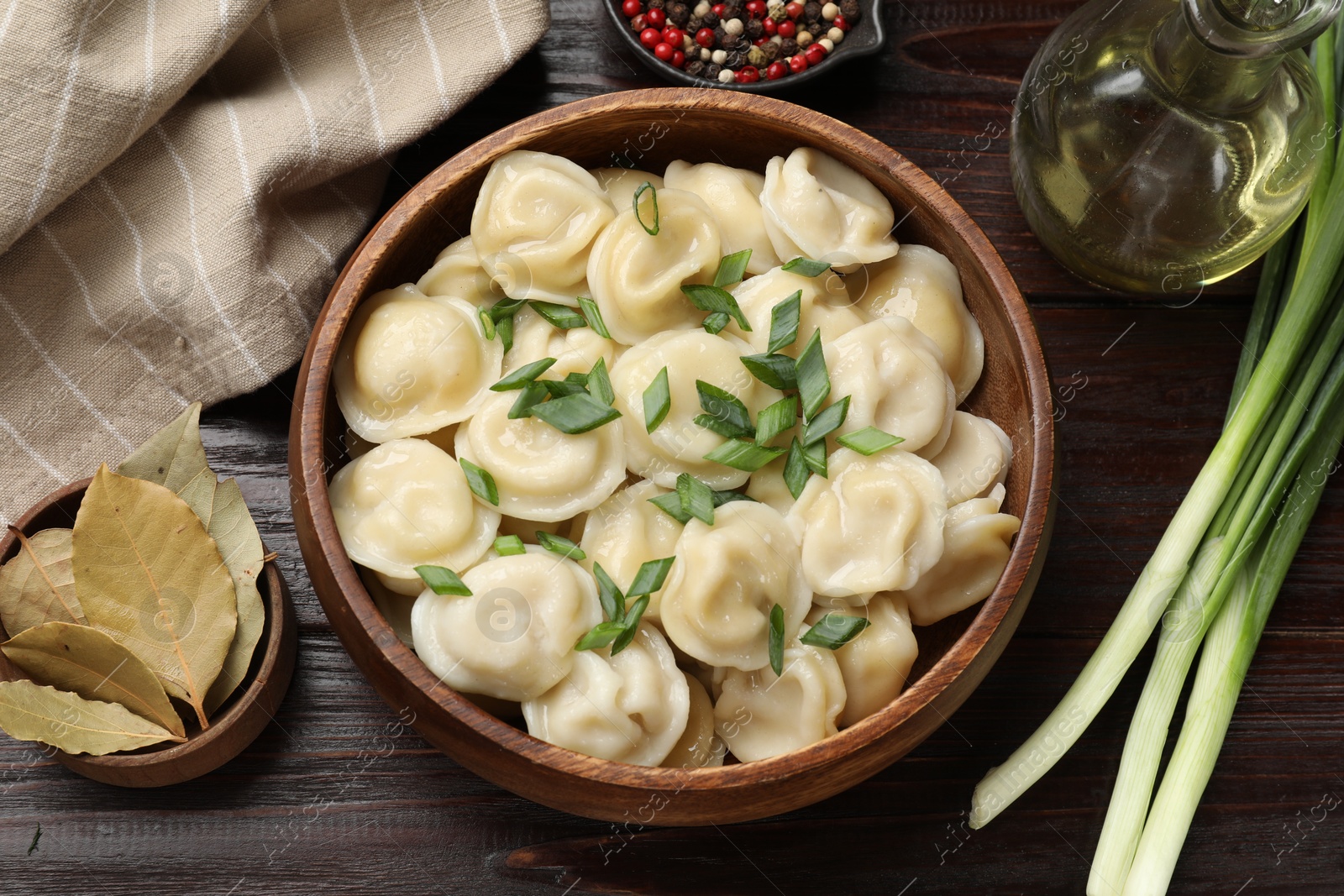 Photo of Delicious pelmeni with green onion, spices and oil on wooden table, flat lay