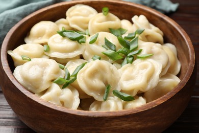 Delicious pelmeni with green onion in bowl on table, closeup