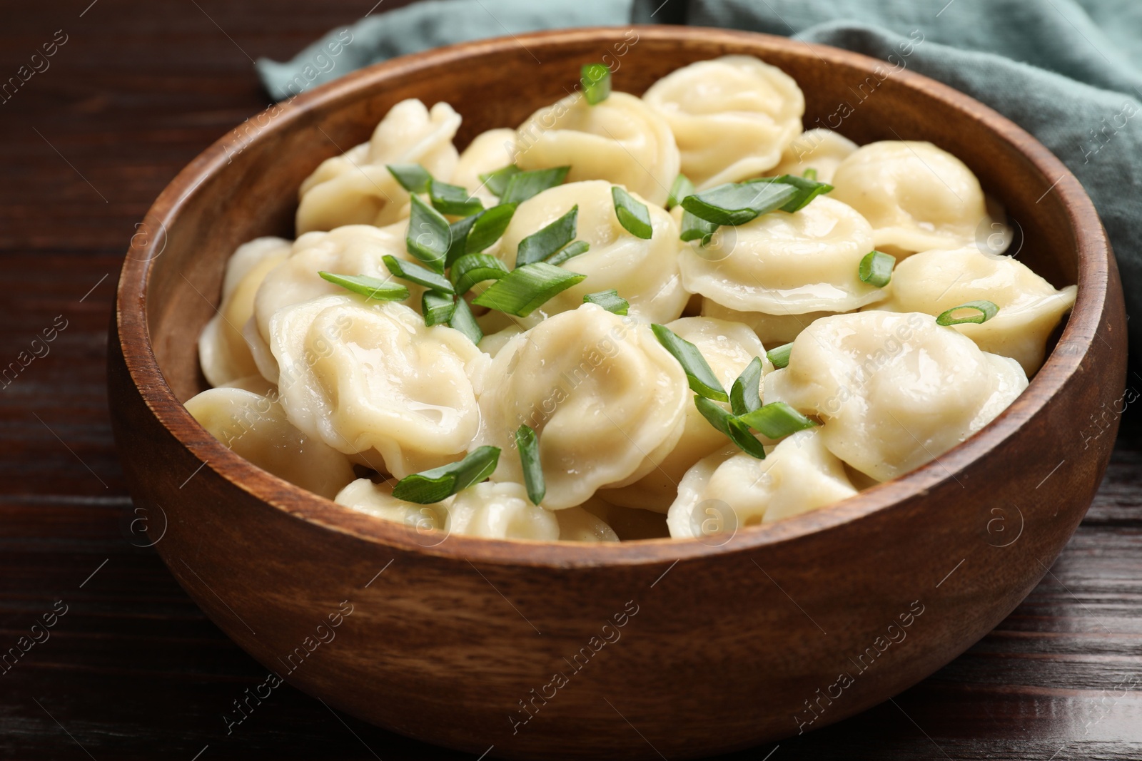 Photo of Delicious pelmeni with green onion in bowl on wooden table, closeup